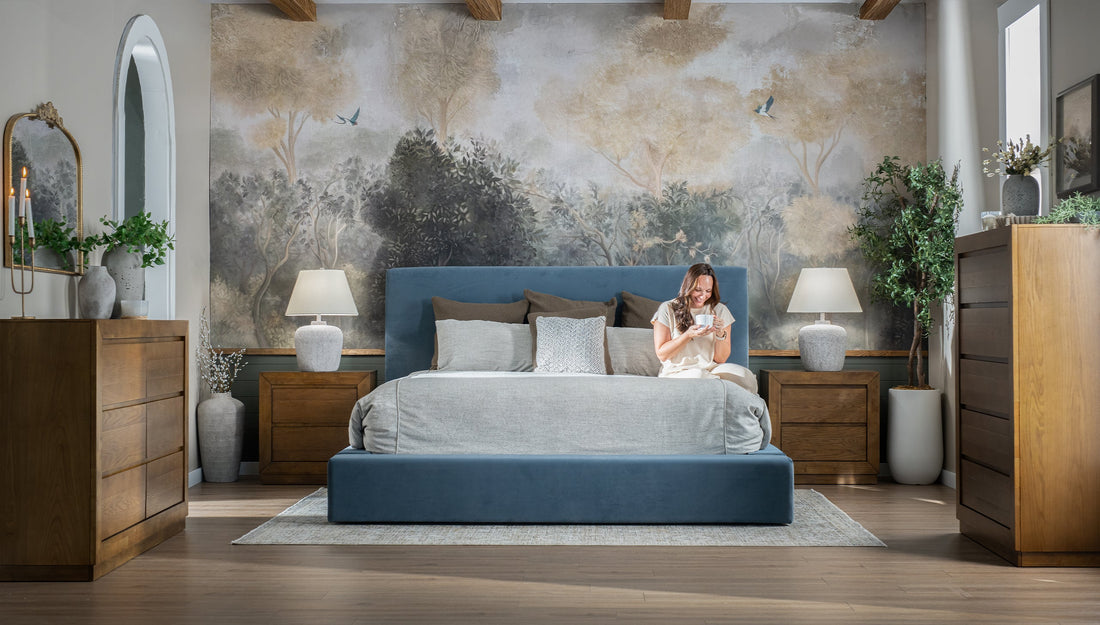 A woman sitting on her bed in a bedroom with wallpaper.