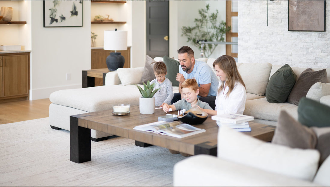 A family sitting around a coffee table in a living room with white furniture.