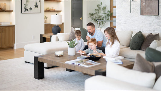 A family sitting around a coffee table in a living room with white furniture.