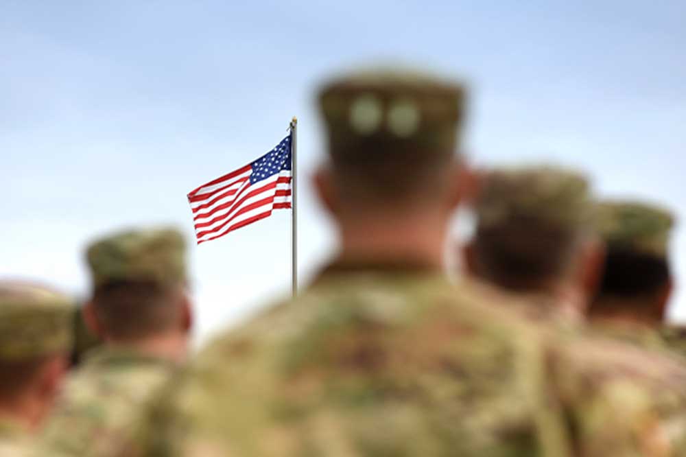 Soldiers in uniform facing an American flag